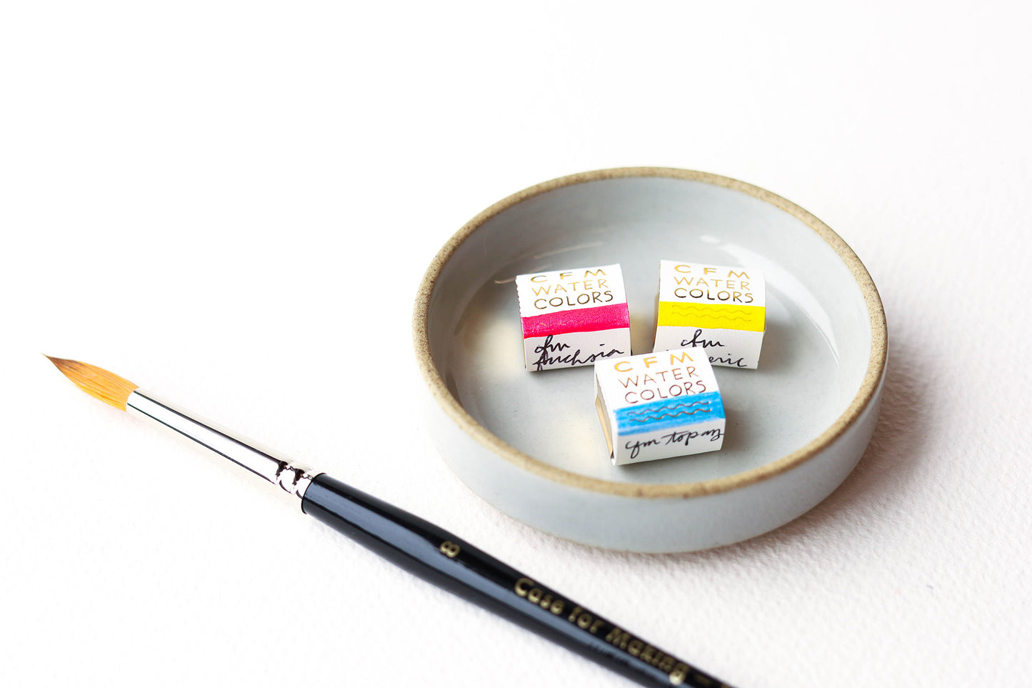 Three Case for Making handmade watercolors in a ceramic Hasami Dish with a Round Size 8 CfM Watercolor brush, photo from side angle.