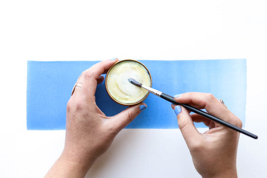 An open Case for Making Brush Buddy in the process of being used. Two hands shown, one holding the circular brush buddy and the other holding the brush being cleaned.