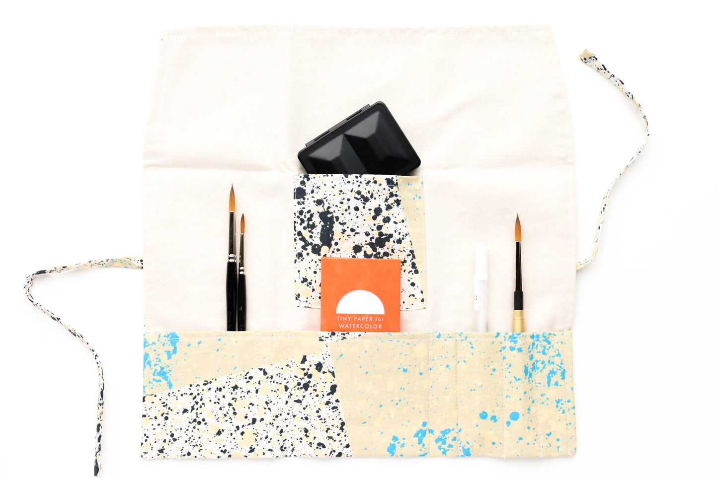 The open Terrasse pattern brush roll shown with a sampling of brushes, a simple travel palette, and a tiny paper pack.