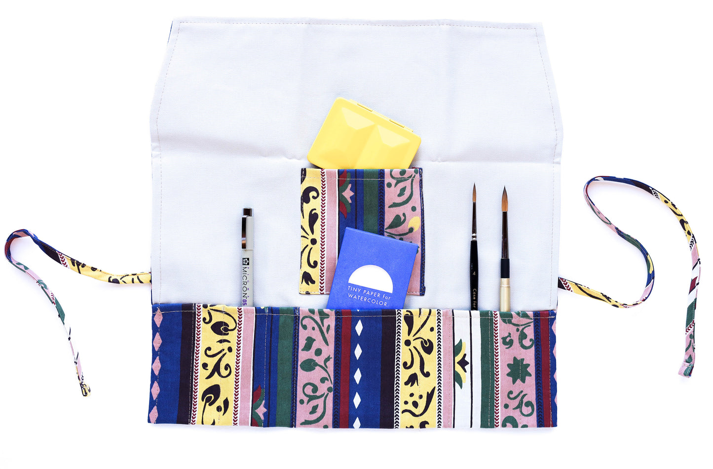 The open Pulcinella pattern brush roll shown with a sampling of brushes, a pen, a simple travel palette, and a tiny paper pack.