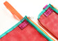 Close-up of two mesh zip pouches in bright coral red with teal trim and orange webbing handles, both showing a purple Buena Goods brand tag.