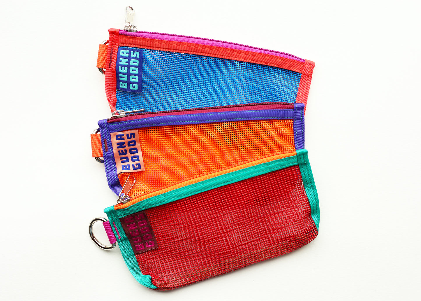 Three mesh bags by buena goods on a white background. The bags are red with green trim, orange with purple trim and blue with red trim. They all have colorful zippers.