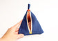 A hand holding a small triangular blue fabric pouch with a top loop and an open gold zipper showing an orange patterned lining, against a plain white background.