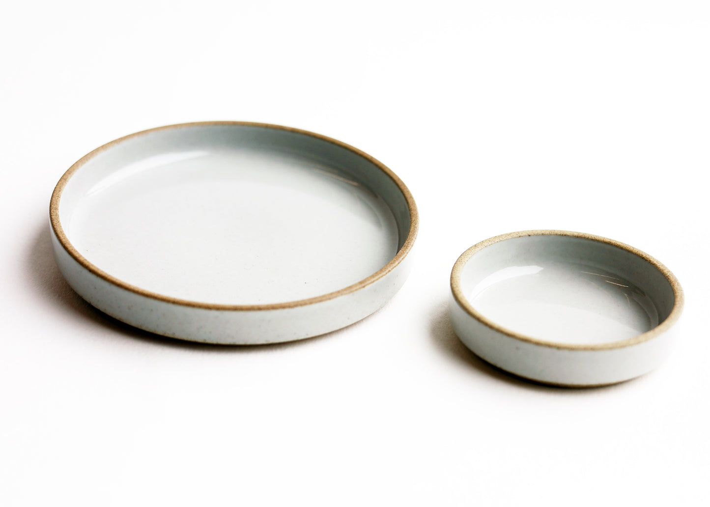 Two round ceramic shallow dishes in a light gray glaze with a natural tan rim, shown on a clean white background.