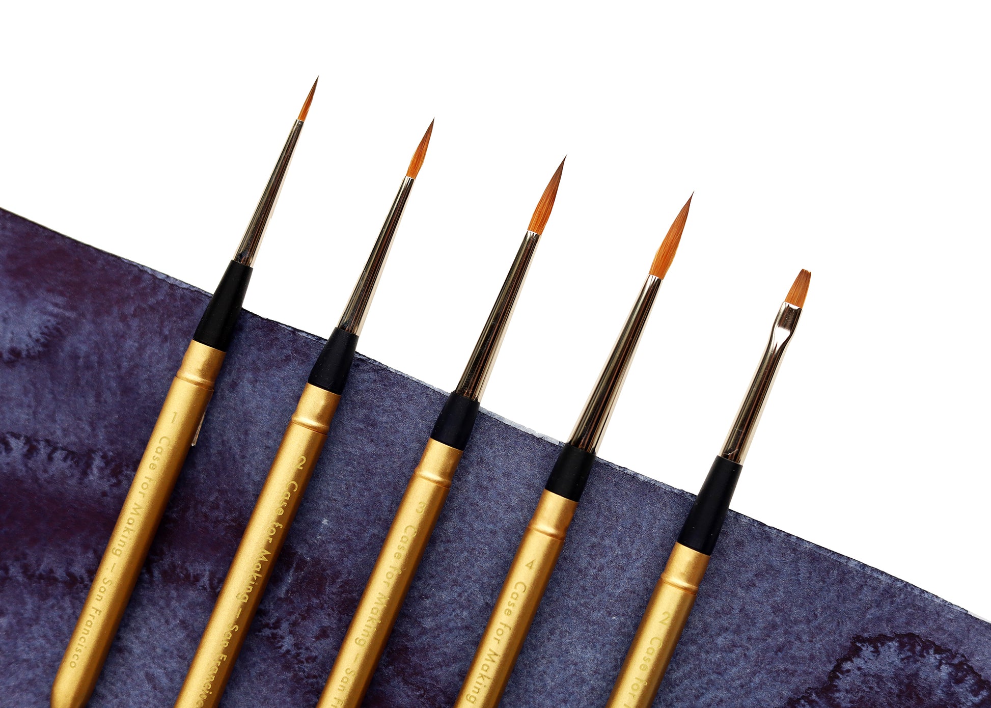 A detail close-up of 5 mini travel brushes lined up on an indigo watercolor swipe.