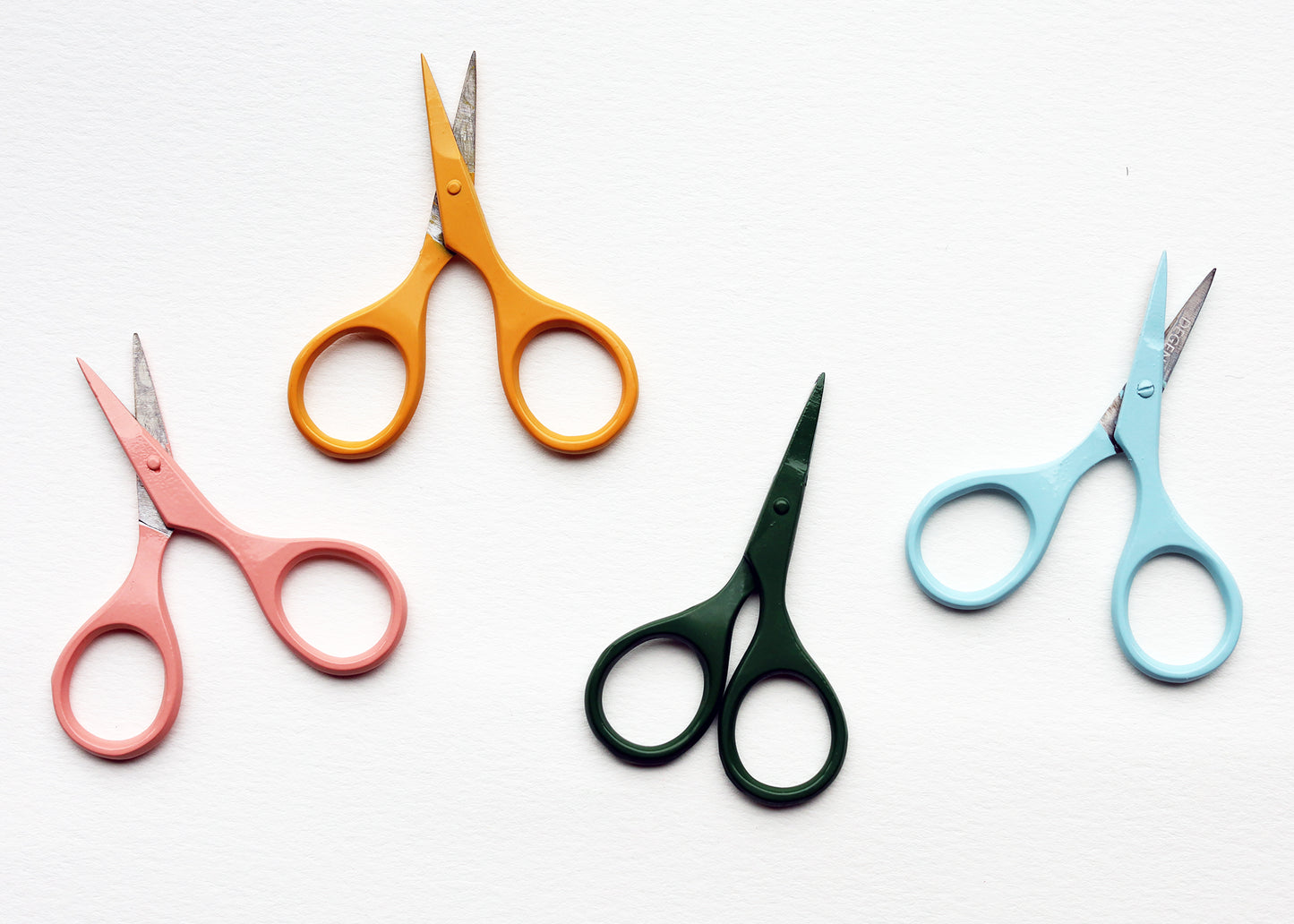 Four pairs of small scissors with colorful handles in orange, pink, dark green, and light blue, arranged on a white background.