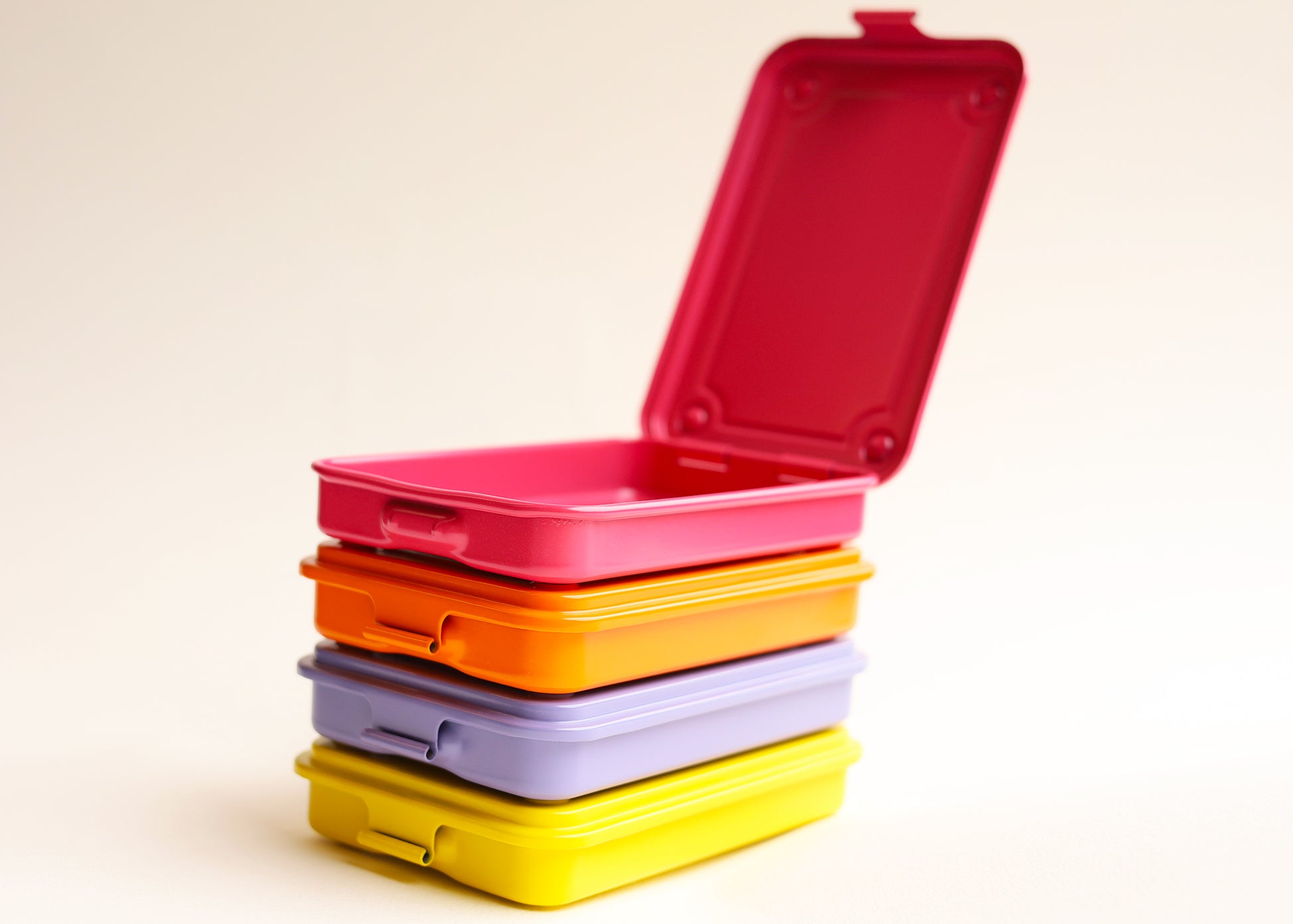 A stack of four rectangular stamped metal storage in bright pink, orange, lilac, and yellow, photographed on a clean white background. The top box is open.