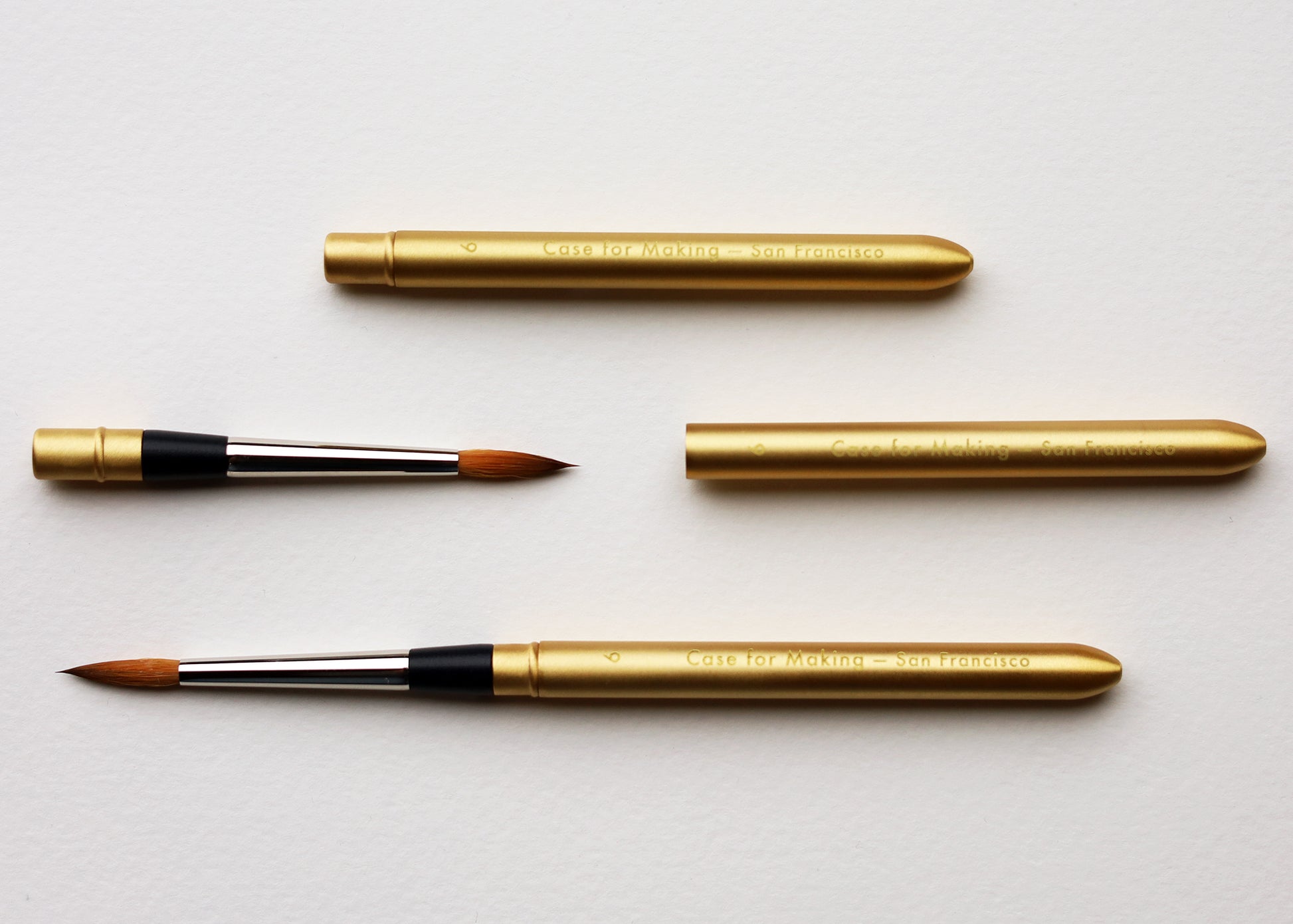 Four gold watercolor brushes and brushes with black ferrules and brown bristles, arranged on a clean white background showing how the brushes folds and closes to protect the brush tip.