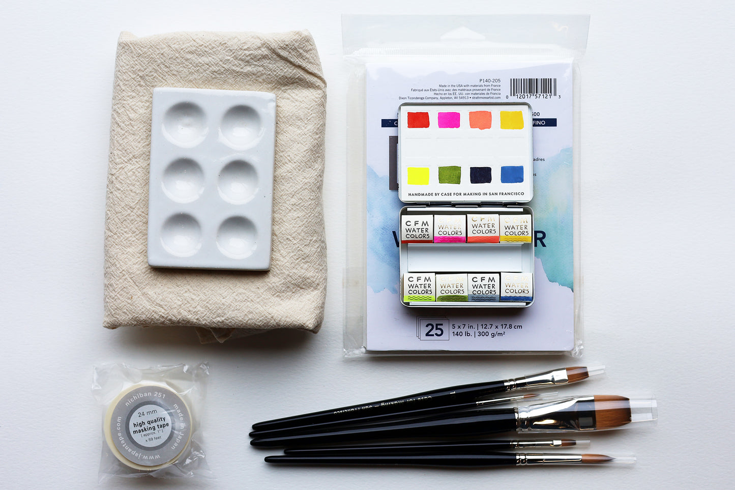 An image of watercolor supplies on a white background including 5 brushes, a watercolor palette, paper, mixing palette, tape and dish cloth.