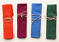 Four rolled fabric napkins in orange, raspberry, blue, and green, each tied with a beige leather string and shown on a white background.
