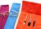 An orange fabric art supply roll with several pockets holding paintbrushes and a pen, shown next to purple and blue rolls tied with cord on a white background.
