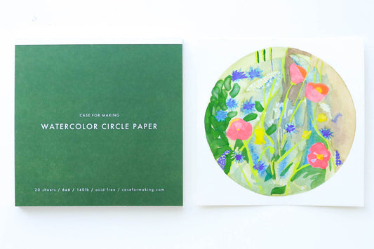 The closed, top-bound 6" x 6" Watercolor Circle Paper pad.  Showing the forest green cover with white lettering.  Also shown is a painted sample sheet of the Circle Paper.