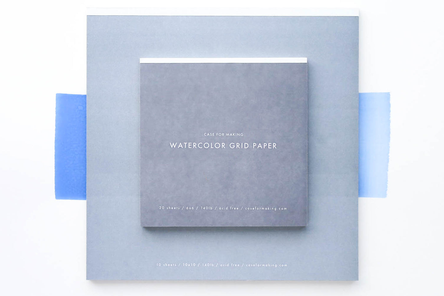 The closed, top-bound 6" x 6" and 10" x 10" Watercolor Grid Paper pads.  Showing the soft greycover with white lettering. 