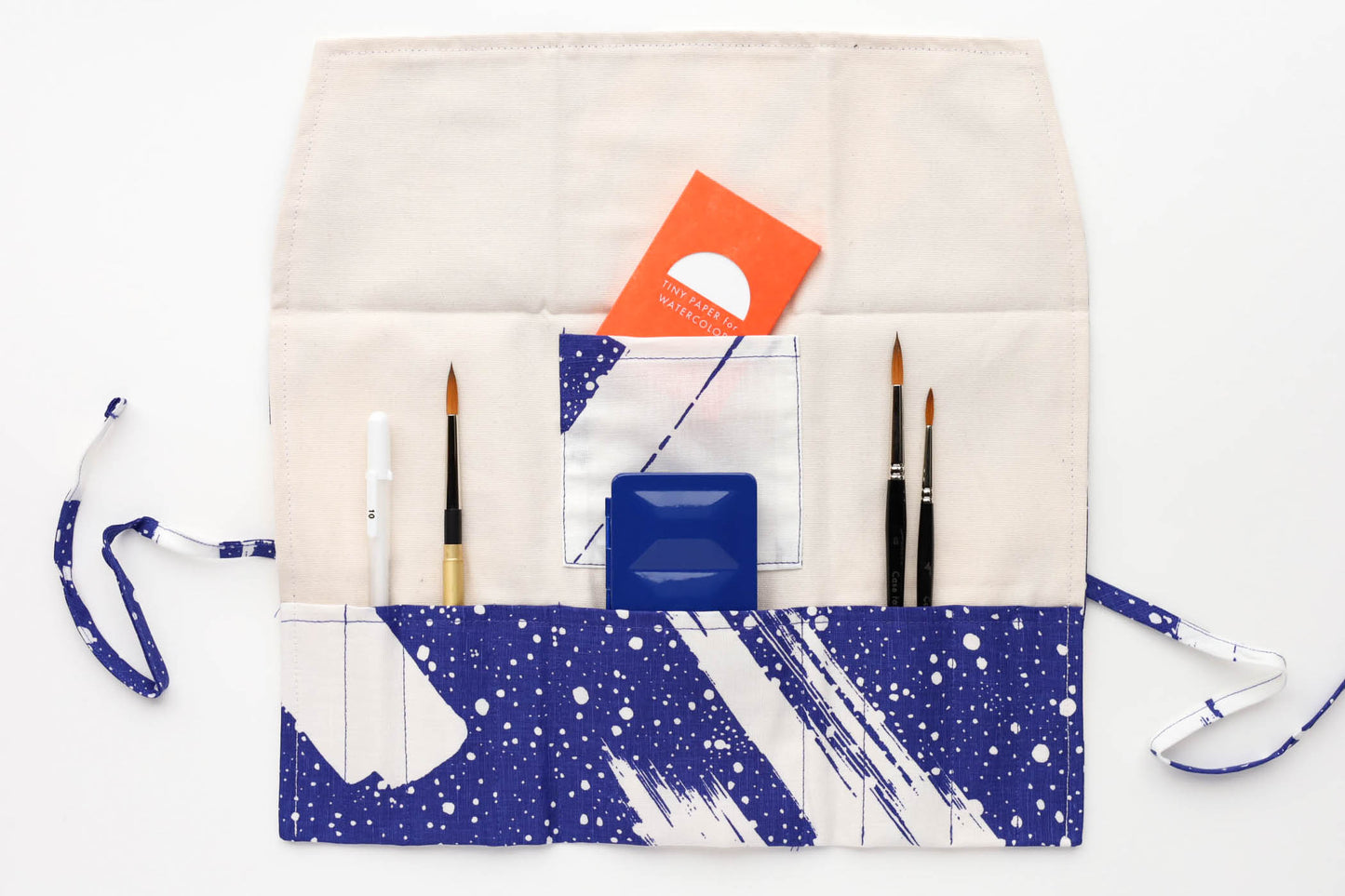 The open Accord Comet pattern brush roll shown with a sampling of brushes, a simple travel palette, and a tiny paper pack.