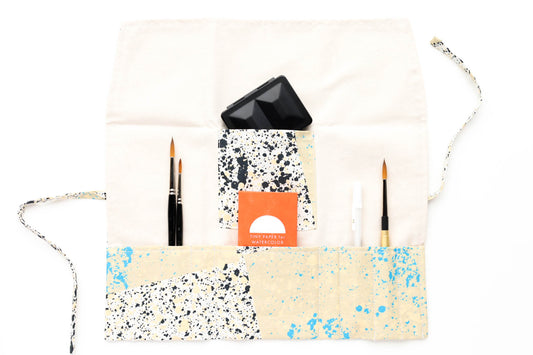 The open Terrasse pattern brush roll shown with a sampling of brushes, a simple travel palette, and a tiny paper pack.