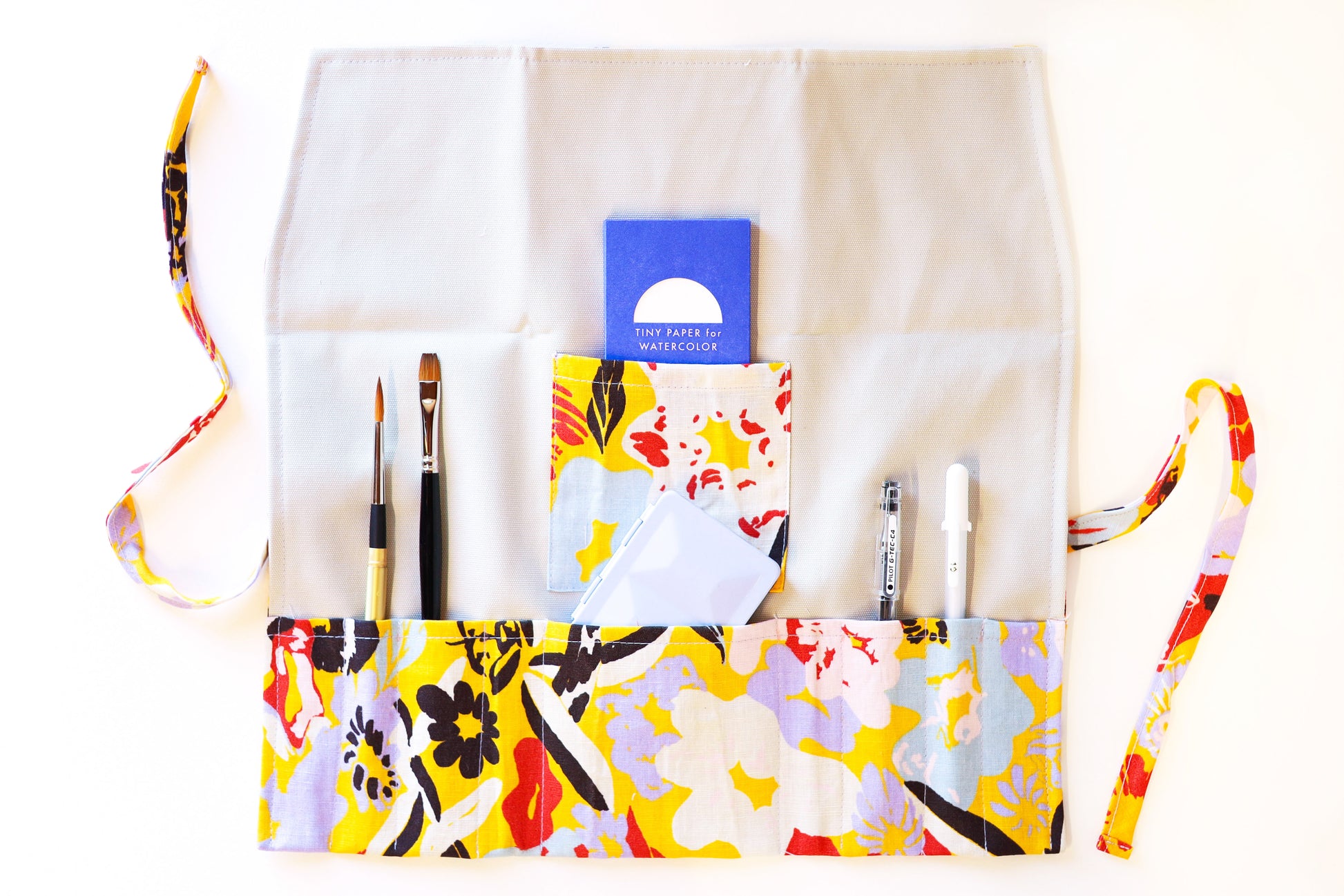 The open Primo Pitino pattern brush roll shown with a sampling of brushes, pens, a simple travel palette, and a tiny paper pack.