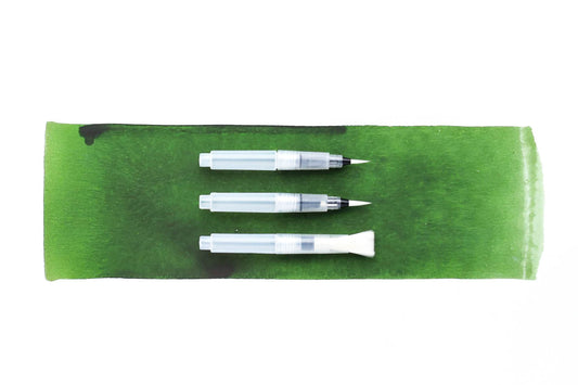 Three water brushes with caps off showing the tips sizes - two sizes of round and one large flat brush